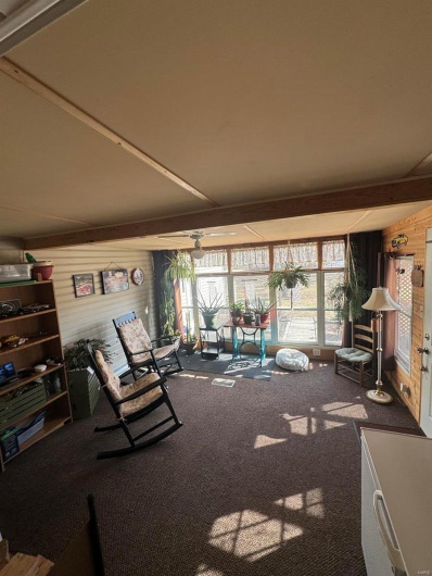 Unfurnished living room with carpet floors, beamed ceiling, a sunroom, and wooden walls