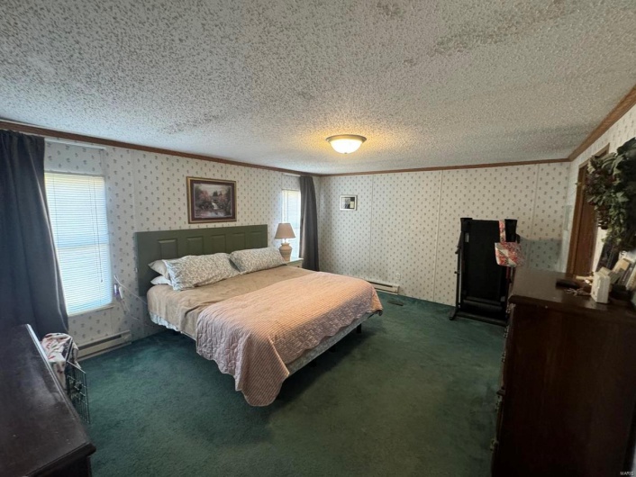 Bedroom featuring ornamental molding, dark carpet, a textured ceiling, and wallpapered walls