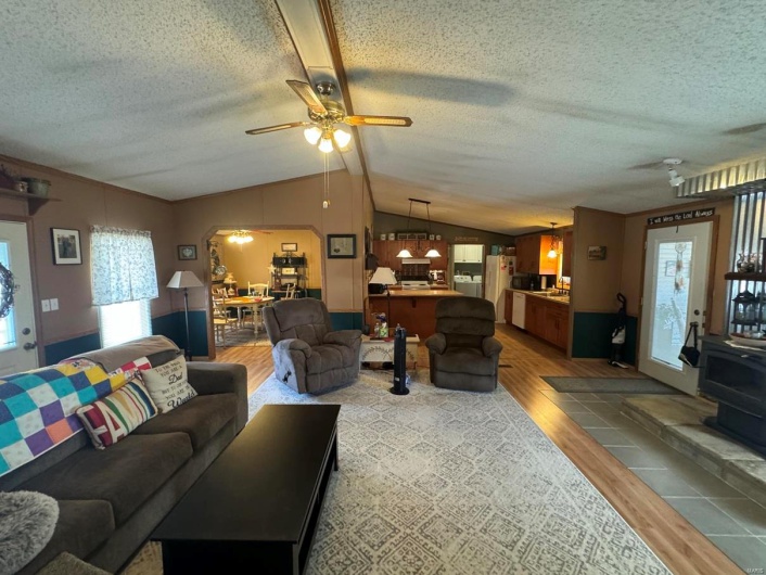 Living area with arched walkways, a wood stove, vaulted ceiling, ceiling fan, and light wood-type flooring
