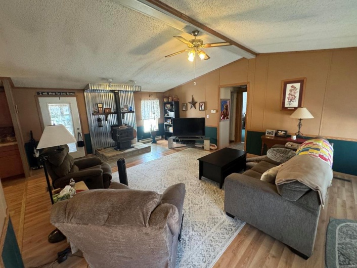 Living room with lofted ceiling with beams, a wood stove, a textured ceiling, and wood finished floors
