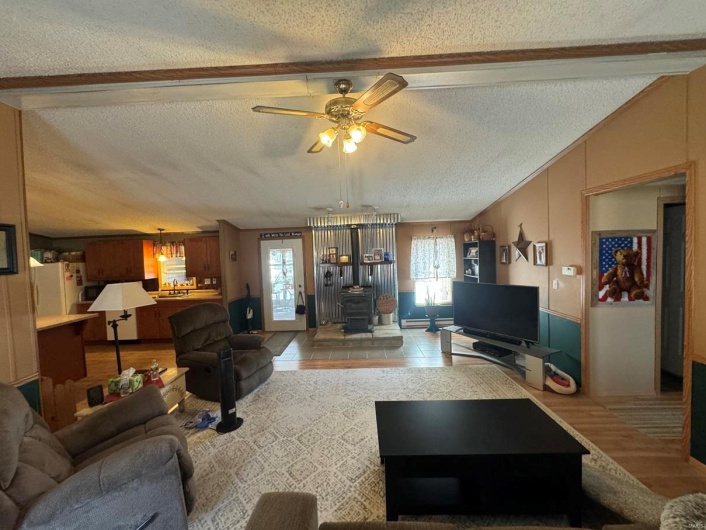Living area with lofted ceiling, a wood stove, ceiling fan, and a textured ceiling