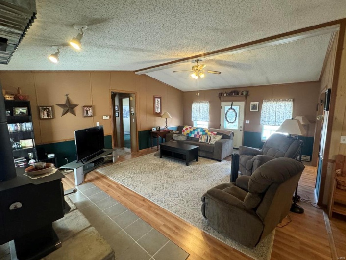 Living area featuring a ceiling fan, plenty of natural light, vaulted ceiling, and wood finished floors
