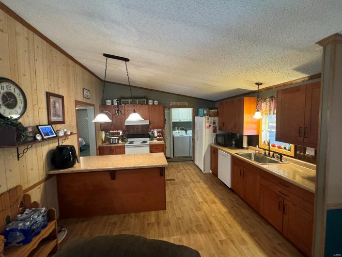 Kitchen featuring lofted ceiling, light wood-style flooring, a sink, white appliances, and a peninsula