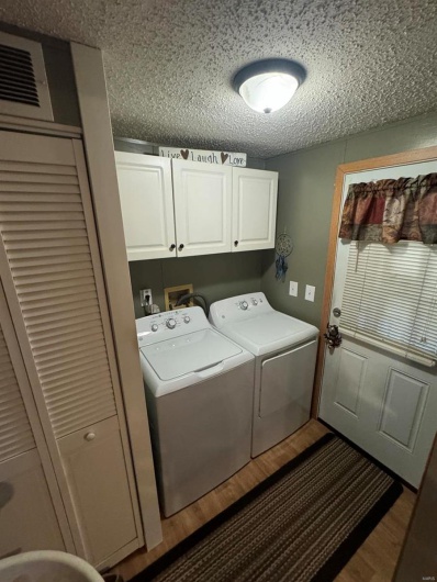 Washroom with cabinet space, washing machine and dryer, a textured ceiling, and wood finished floors