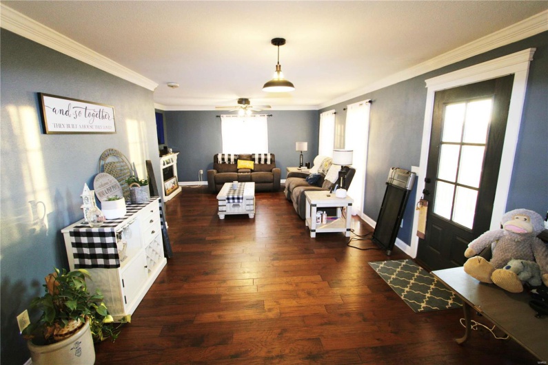 Living area featuring dark wood-type flooring, a fireplace, a ceiling fan, baseboards, and crown molding