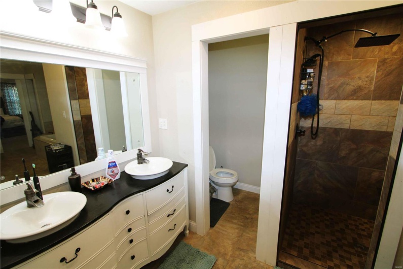 Bathroom featuring toilet, double vanity, a sink, and tiled shower
