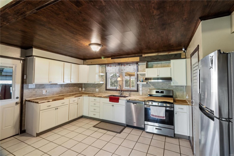 Kitchen with under cabinet range hood, stainless steel appliances, wooden ceiling, a sink, and decorative backsplash