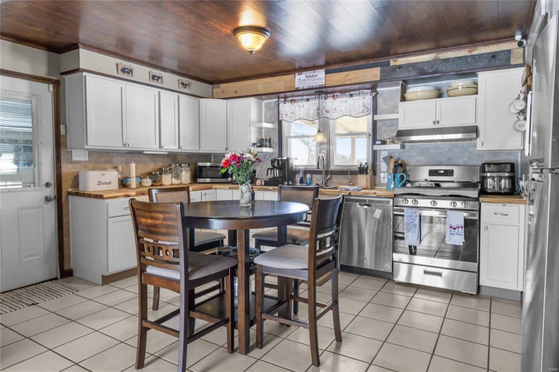 Kitchen with appliances with stainless steel finishes, white cabinets, light tile patterned flooring, wood counters, and under cabinet range hood