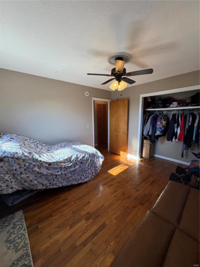Bedroom with a textured ceiling, ceiling fan, a closet, and wood finished floors
