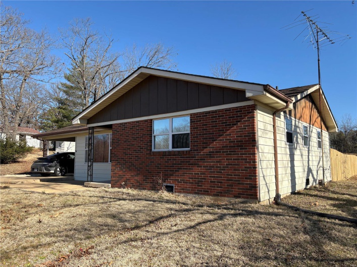 View of side of home featuring board and batten siding, an attached carport, concrete driveway, and brick siding