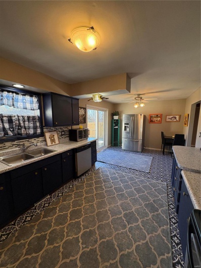 Kitchen with a ceiling fan, dishwashing machine, dark cabinets, fridge, and a sink