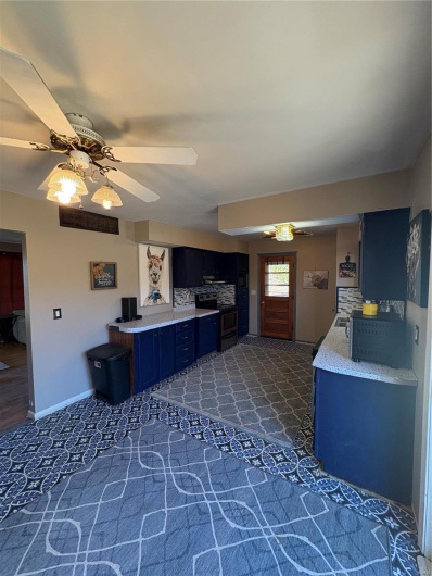 Kitchen with tasteful backsplash, ceiling fan, stove, blue cabinets, and light countertops