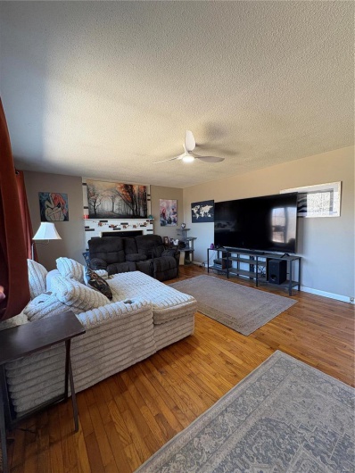 Living area with ceiling fan, a textured ceiling, baseboards, and wood finished floors