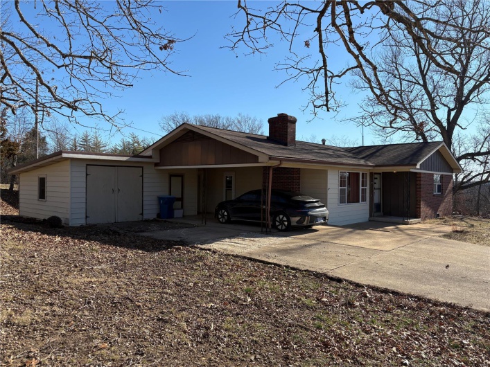 View of front of home featuring a carport, concrete driveway, brick siding, and a chimney