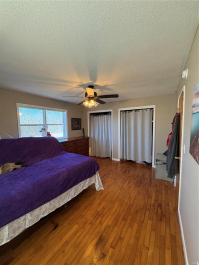 Bedroom with a textured ceiling, hardwood / wood-style flooring, a ceiling fan, baseboards, and multiple closets