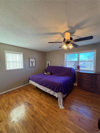 Bedroom featuring a textured ceiling, ceiling fan, hardwood / wood-style flooring, and baseboards