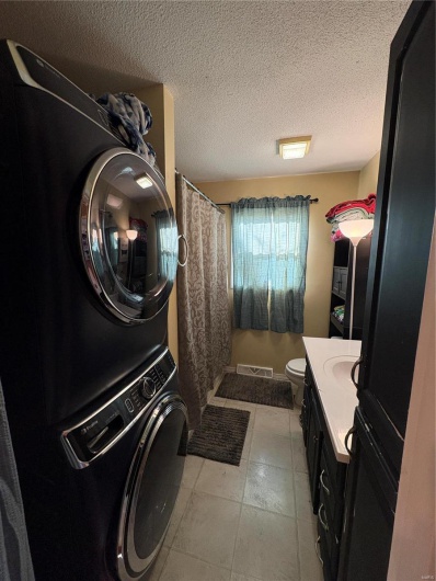 Washroom with light tile patterned floors, visible vents, a sink, a textured ceiling, and stacked washing maching and dryer
