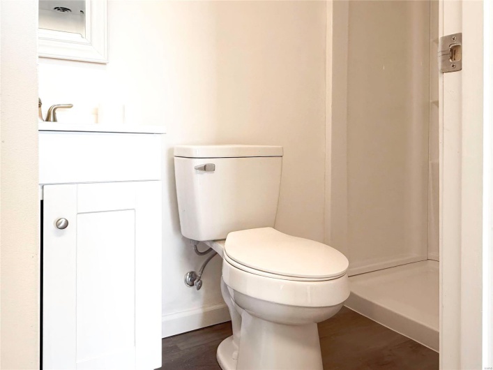 Bathroom featuring baseboards, a shower, toilet, wood finished floors, and vanity