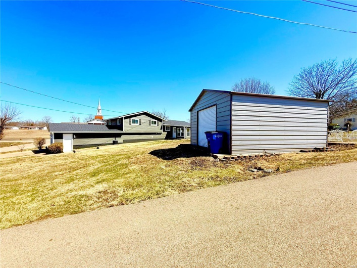 View of side of property featuring a garage, a lawn, and an outdoor structure