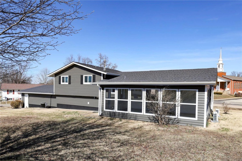 Back of house with central AC unit, roof with shingles, and a sunroom