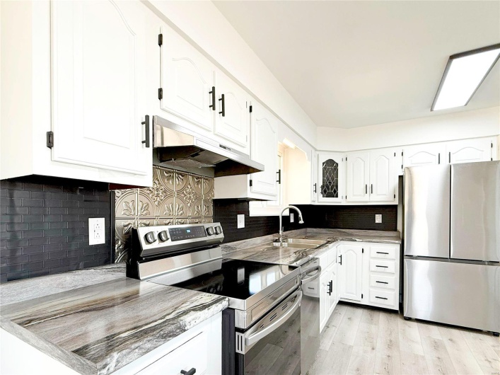 Kitchen with white cabinets, light wood-style floors, stainless steel appliances, under cabinet range hood, and a sink