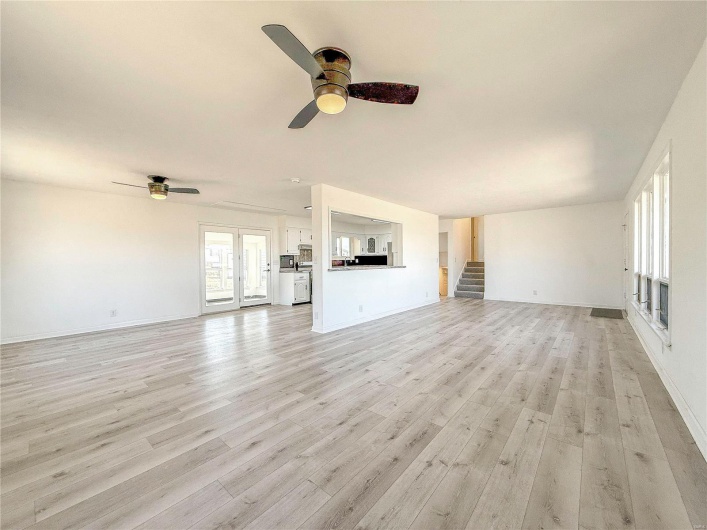 Unfurnished living room featuring light wood-style floors, a ceiling fan, baseboards, and stairs