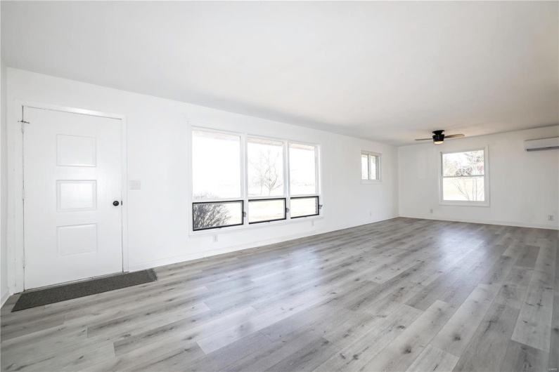 Unfurnished living room featuring light wood-type flooring, a wall mounted air conditioner, ceiling fan, and baseboards