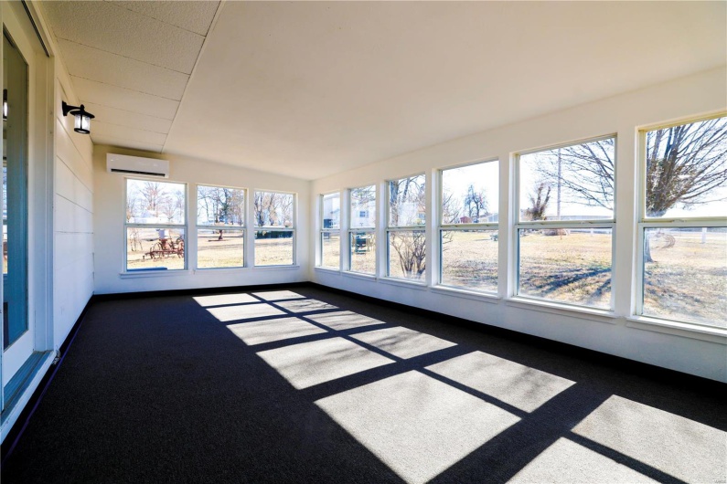 Unfurnished sunroom with plenty of natural light and a wall mounted air conditioner