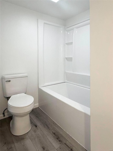 Full bathroom featuring baseboards, toilet, and wood finished floors