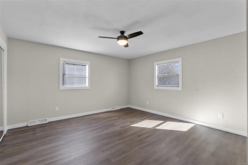 Spare room with dark wood-style floors, ceiling fan, visible vents, and baseboards