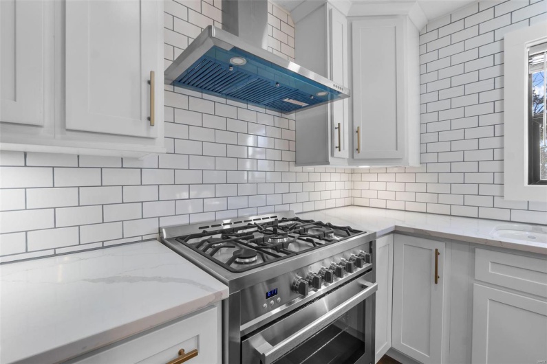 Kitchen with tasteful backsplash, wall chimney exhaust hood, light stone counters, high end stainless steel range, and white cabinetry