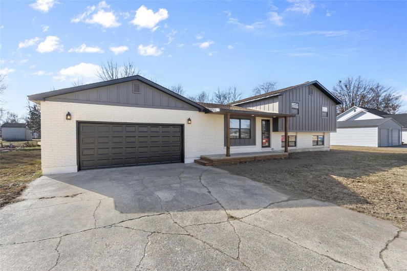 View of front of home with a porch, a garage, brick siding, concrete driveway, and board and batten siding