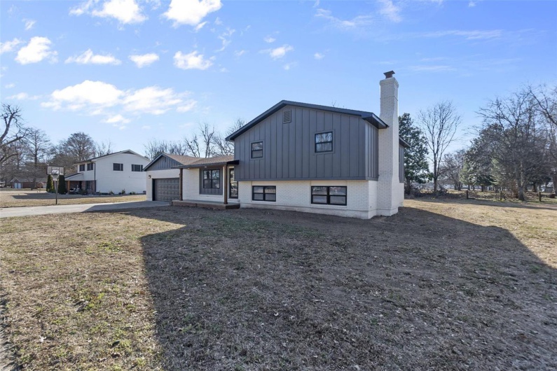 View of front facade featuring driveway, a chimney, an attached garage, board and batten siding, and brick siding