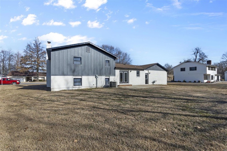 Rear view of house featuring a chimney, a yard, a patio area, board and batten siding, and brick siding