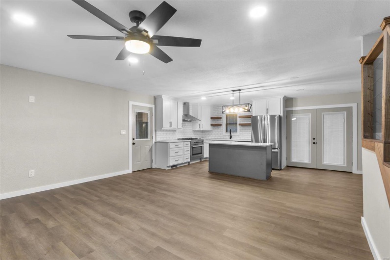 Kitchen with wall chimney exhaust hood, a kitchen island, appliances with stainless steel finishes, light countertops, and open shelves