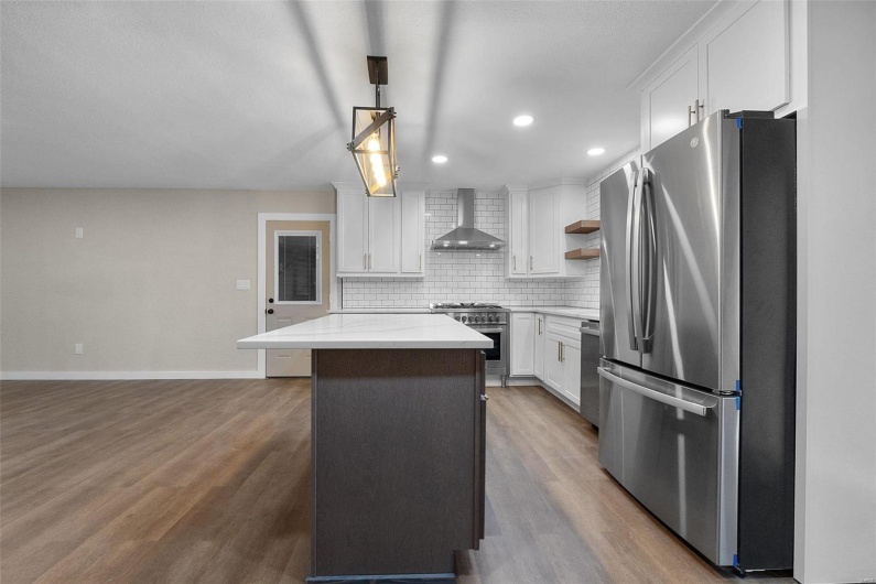 Kitchen featuring a center island, tasteful backsplash, appliances with stainless steel finishes, wall chimney range hood, and wood finished floors
