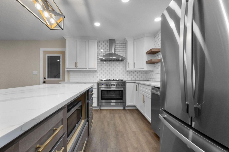 Kitchen featuring open shelves, stainless steel appliances, decorative backsplash, wall chimney range hood, and wood finished floors