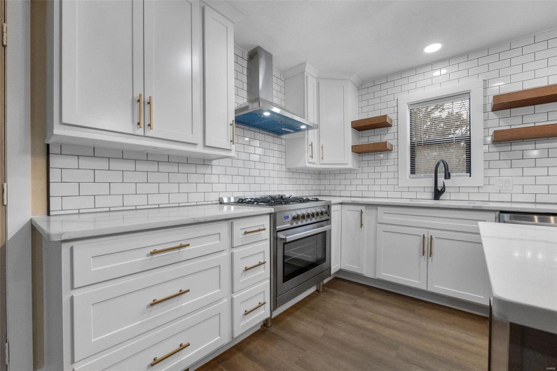 Kitchen with dark wood-style flooring, stainless steel range, open shelves, a sink, and wall chimney range hood