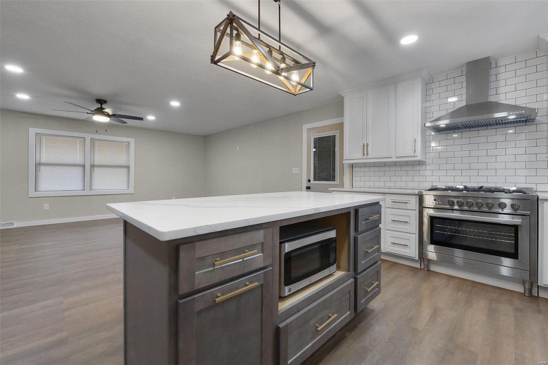 Kitchen with wall chimney range hood, dark wood-type flooring, appliances with stainless steel finishes, and white cabinets