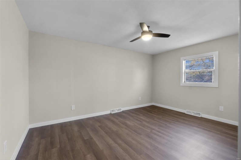Empty room with dark wood-style flooring, visible vents, and baseboards