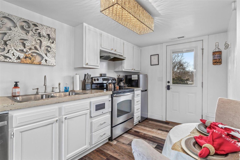 Kitchen with under cabinet range hood, a sink, white cabinetry, appliances with stainless steel finishes, and dark wood finished floors