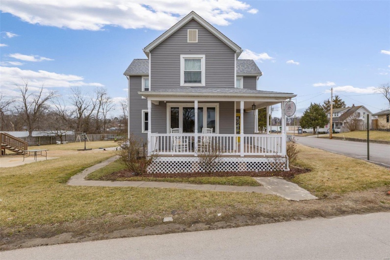View of front facade with a porch, roof with shingles, and a front yard