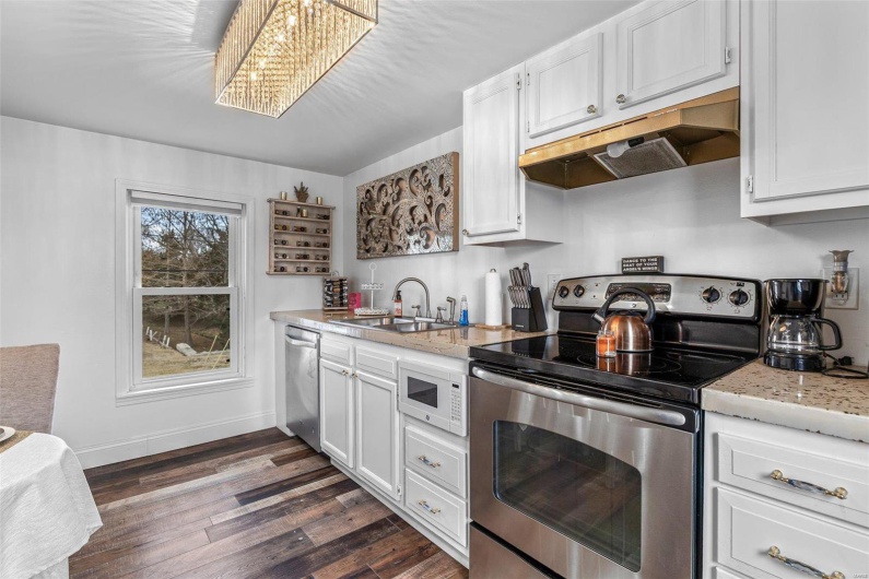 Kitchen featuring white cabinets, dark wood-type flooring, stainless steel appliances, under cabinet range hood, and a sink