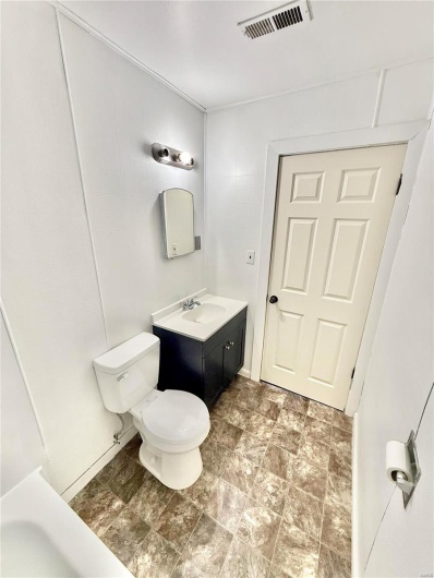 Bathroom with stone finish floor, visible vents, vanity, and toilet