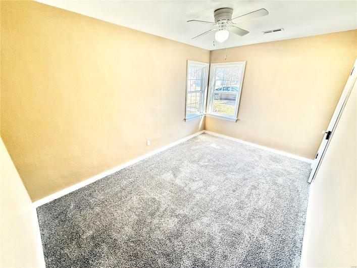 Carpeted empty room featuring ceiling fan, visible vents, and baseboards
