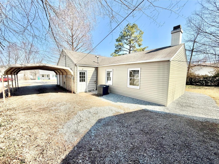 Rear view of property with gravel driveway, a chimney, a shingled roof, a detached carport, and central AC