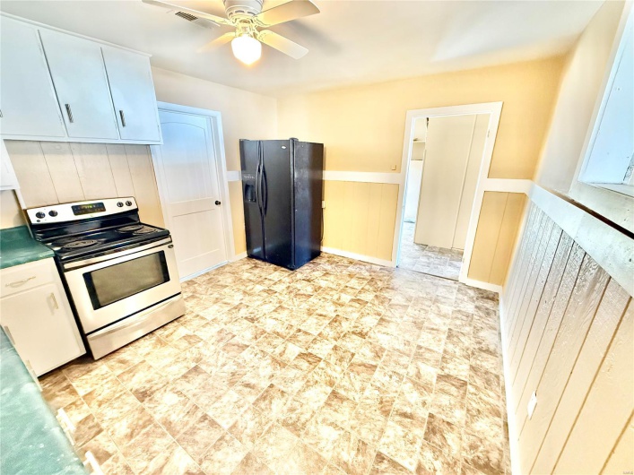 Kitchen with ceiling fan, a wainscoted wall, visible vents, stainless steel range with electric cooktop, and black refrigerator with ice dispenser