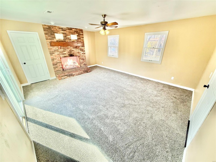 Living room with visible vents, baseboards, ceiling fan, carpet, and a brick fireplace