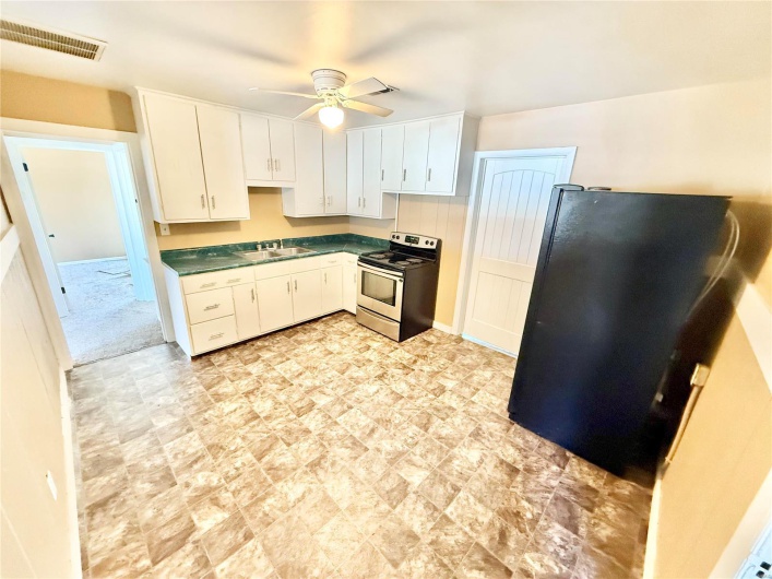 Kitchen featuring dark countertops, visible vents, freestanding refrigerator, a sink, and stainless steel electric range