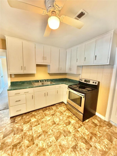 Kitchen with ceiling fan, electric range, visible vents, white cabinetry, and dark countertops